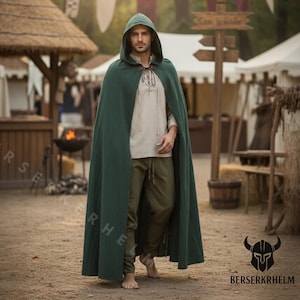 May include: A dark green hooded cloak with a leather clasp, worn over a light-colored shirt and olive-green pants. The cloak is long and flowing, with a deep hood. The background shows a medieval fair setting.