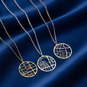 Könnte beinhalten: Drei Halsketten mit Anhängern im Karten-Design. Eine ist goldfarben mit einem roten Edelstein, eine silberfarben mit einem grünen Edelstein und eine roségoldfarben mit einem blauen Edelstein. Die Anhänger haben feine Ketten, vor einem dunkelblauen Hintergrund.