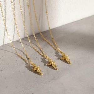 Puede incluir: Varias cadenas doradas con colgantes de &aacute;ngeles. Las cadenas son delicadas, con peque&ntilde;os detalles de cuentas. Cada colgante de &aacute;ngel est&aacute; detallado con alas y vestiduras fluidas. Se exhiben sobre una superficie gris claro.