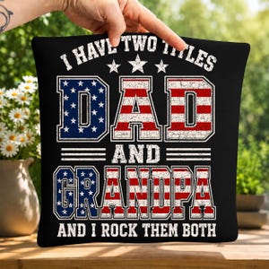 Può includere: Cuscino quadrato nero con la scritta "I HAVE TWO TITLES DAD AND GRANDPA AND I ROCK THEM BOTH" in bianco, rosso e blu. Le parole "DAD" e "GRANDPA" sono disegnate con un tema della bandiera americana.