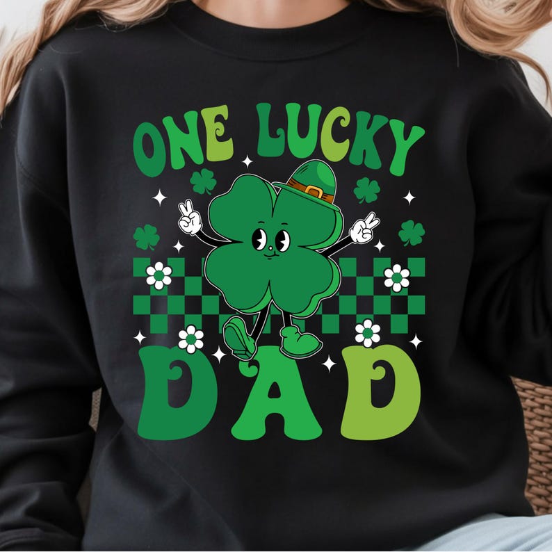 May include: Black sweatshirt with a St. Patrick's Day design. The graphic features a green four-leaf clover character wearing a hat and making a peace sign. The text reads "ONE LUCKY DAD" in green.
