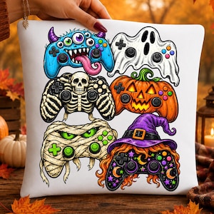 Op de afbeelding: Een wit vierkant kussen met een grafische print van zes videogamecontrollers in Halloween-thema. De ontwerpen bevatten een blauw monster, een witte geest, een skelet, een oranje pompoen, een mummie en een controller in heksenthema.