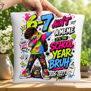 May include: A white square pillow featuring a colorful graphic of a child wearing sunglasses and a hoodie, surrounded by paint splatters and text that reads 6-7 AIN'T A MEME IT'S THE SCHOOL YEAR BRUH 2026-2027 with a checklist of goals including learn, grow, win.