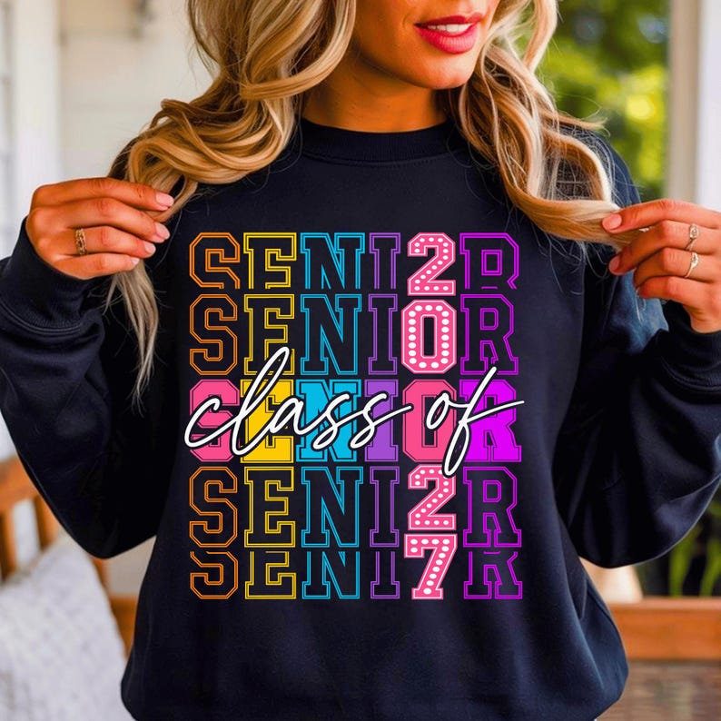May include: Black sweatshirt featuring the text "SENIOR 2023" in a vibrant, layered design. The words "class of" are written in a cursive font across the centre. The sweatshirt is a casual style.