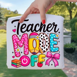 Puede incluir: Cojín blanco con la frase "Teacher MODE OFF" en un diseño colorido. El diseño incluye un lápiz, una manzana, libros y un lazo rosa. Las letras están en varios patrones y colores, incluyendo estampado de leopardo rosa y lunares blancos y negros.