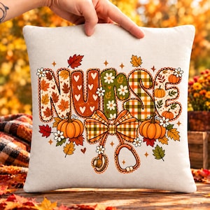 Op de afbeelding: Een vierkant gebroken wit sierkussen met het woord NURSE in grote, decoratieve letters gevuld met herfstpatronen zoals herfstbladeren, witte hartjes, groen ruitpatroon en madeliefjes, geaccentueerd door oranje pompoenen en een stethoscoop.