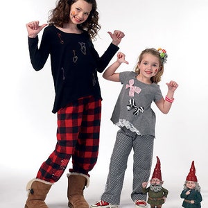 May include: Two young people wearing matching outfits. One wears a black long-sleeve shirt with embroidered designs and red and black plaid pants. The other wears a gray top with bows and gray polka dot pants. Two garden gnomes stand nearby.