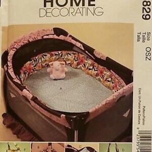 May include: A sewing pattern for a playpen with a pink and floral print. The pattern includes instructions for making a playpen, a fitted sheet, and a tote bag. The pattern number is M5829.