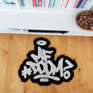 May include: A black and white rug featuring the text "#F DOOM?". The rug has a black border and the text is in a graffiti-style font. The rug is placed on a wooden floor.