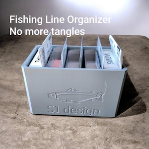 May include: A light blue fishing line organizer with the text "Fishing Line Organizer No more tangles". The organizer has a fish design and the text "SJ design". It holds several spools of fishing line.