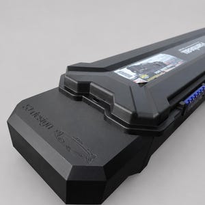 May include: A black, elongated, hard-shell carrying case with a moulded geometric design. The case features the embossed text "ST design" and a fish graphic on the end, with a rectangular product label and blue latch details visible along the side.