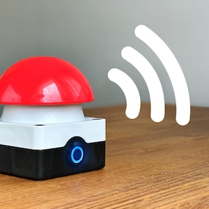 May include: A red button with a white base and a black box with a blue light. The button is on a wooden surface and there is a white wifi symbol in the background.