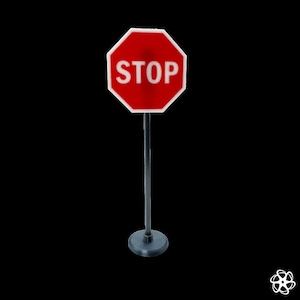 Puede incluir: Un pequeño letrero de stop rojo y blanco con la palabra "STOP" en letras mayúsculas blancas. El letrero octogonal está montado sobre un poste gris con una base circular, sobre un fondo negro.