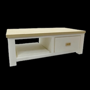 May include: A white coffee table with a light wood top and a drawer. The table has a rectangular shape with a shelf and a drawer with a gold-colored handle. The top is made of light-colored wood.
