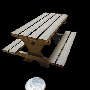 Könnte beinhalten: Ein kleiner Picknicktisch in Hellbraun, mit einer Lattenoberfläche und Bänken sowie einer X-förmigen Stützstruktur. Eine Münze dient als Maßstab. Der Tisch ist etwa 76 cm lang.