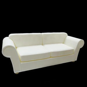 May include: A two-seater white sofa with rounded arms and a low back. The sofa has a simple, classic design and is set against a black background. The cushions appear to be made of a soft, textured material.