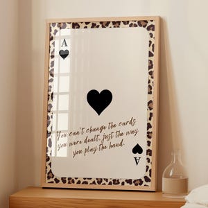 Puede incluir: Impresión artística enmarcada con un diseño de As de Picas. La carta tiene un símbolo de corazón negro y el texto "You can't change the cards you were dealt, just the way you play the hand." El marco tiene un borde con estampado de leopardo.