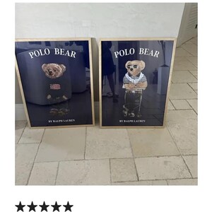 Puede incluir: Dos impresiones enmarcadas con el oso Polo. Cada impresi&oacute;n tiene un fondo azul marino con las palabras "POLO BEAR" en blanco. Un oso lleva un su&eacute;ter con una bandera estadounidense, el otro lleva una camisa a rayas. "BY RALPH LAUREN" est&aacute; impreso debajo.