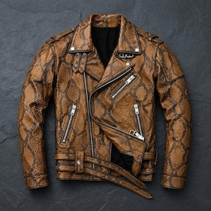 Könnte beinhalten: Eine braune Motorradjacke mit Schlangenledermuster, silberfarbenen Metallreißverschlüssen, einem Reverskragen, Schulterklappen und einem Gürtel mit Schnalle an der Taille. Die Jacke hat ein schwarzes Innenfutter und lange Ärmel mit Reißverschlüssen.