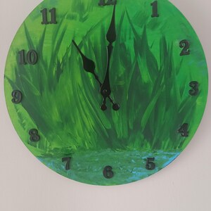 May include: A round green and blue clock with black hands and numbers. The clock face is painted to look like grass.