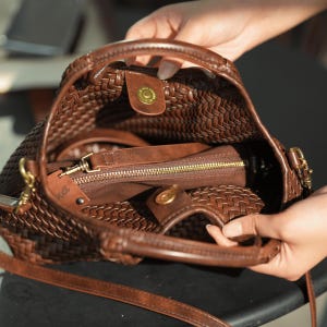Pu&ograve; includere: Una borsa a mano in pelle intrecciata marrone con un manico superiore e una tracolla staccabile. L'interno rivela una pochette con cerniera e una chiusura magnetica a scatto. La borsa ha finiture dorate e una trama intrecciata.