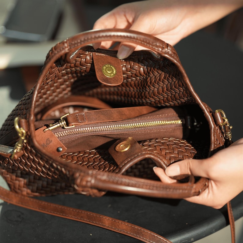 Pu&ograve; includere: Una borsa a mano in pelle intrecciata marrone con un manico superiore e una tracolla staccabile. L'interno rivela una pochette con cerniera e una chiusura magnetica a scatto. La borsa ha finiture dorate e una trama intrecciata.