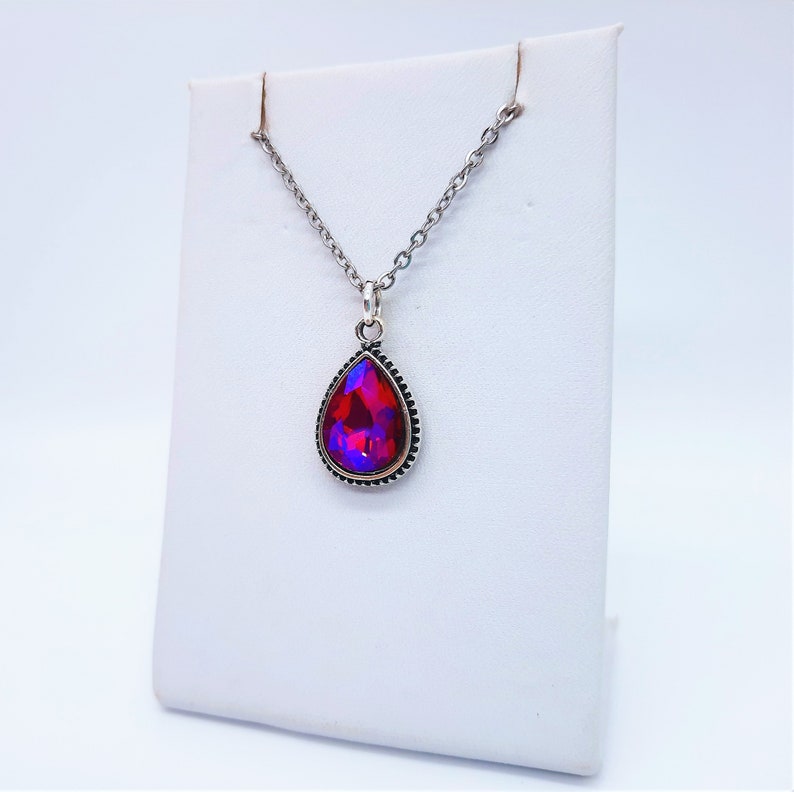 May include: A silver chain necklace with a teardrop-shaped pendant featuring a red and purple iridescent gemstone.