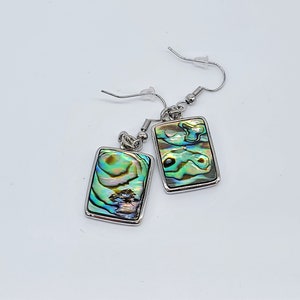 May include: A pair of silver earrings with rectangular abalone shell accents. The shells have a green, blue, and gold iridescent pattern.