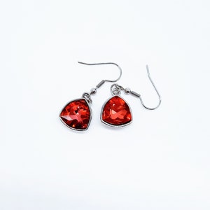 May include: A pair of silver earrings with red gemstone accents. The earrings have a triangular shape and dangle from a silver hook.