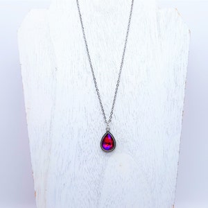 May include: A silver chain necklace with a teardrop-shaped pendant featuring a red and purple iridescent gemstone.