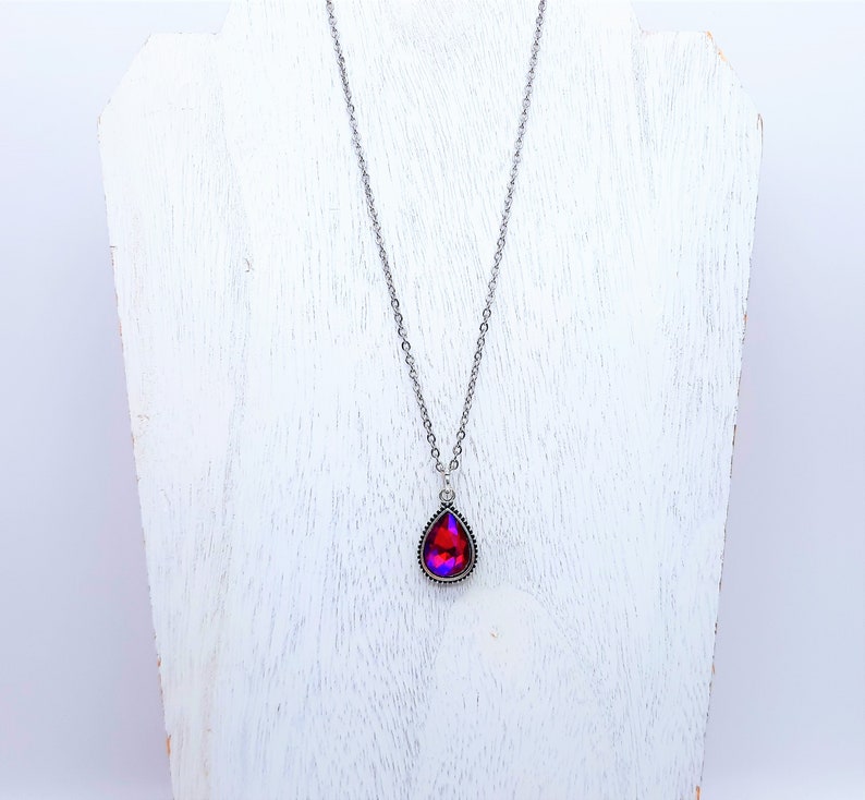 May include: A silver chain necklace with a teardrop-shaped pendant featuring a red and purple iridescent gemstone.
