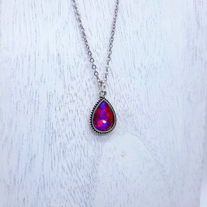 May include: A silver chain necklace with a teardrop-shaped pendant featuring a red iridescent gemstone.