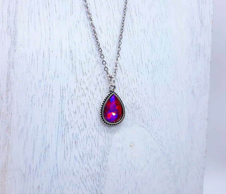 May include: A silver chain necklace with a teardrop-shaped pendant featuring a red iridescent gemstone.