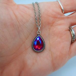 May include: A silver chain necklace with a teardrop-shaped pendant featuring a red iridescent gemstone.