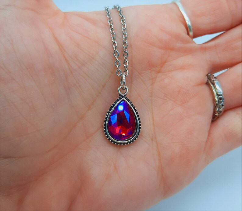 May include: A silver chain necklace with a teardrop-shaped pendant featuring a red iridescent gemstone.