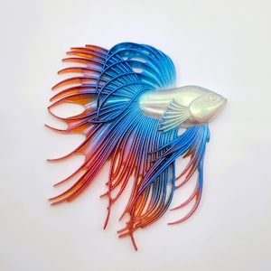 May include: A blue and red iridescent betta fish sculpture with a detailed, layered fin design. The fish is made of a translucent material and has a white iridescent body.