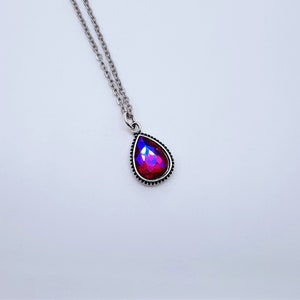 May include: A silver chain necklace with a teardrop-shaped pendant featuring a red iridescent gemstone.