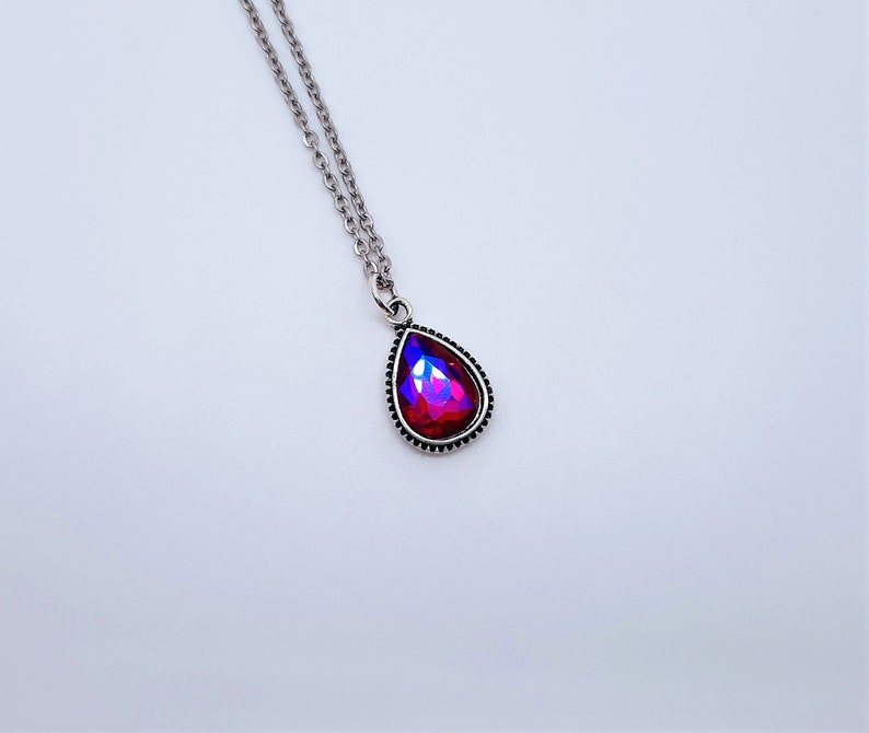 May include: A silver chain necklace with a teardrop-shaped pendant featuring a red iridescent gemstone.