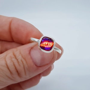 May include: A silver ring with a square-shaped, purple and orange glass stone.
