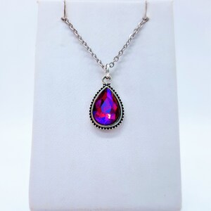 May include: A silver chain necklace with a teardrop-shaped pendant featuring a large, iridescent red and purple gemstone.