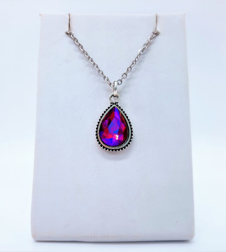 May include: A silver chain necklace with a teardrop-shaped pendant featuring a large, iridescent red and purple gemstone.