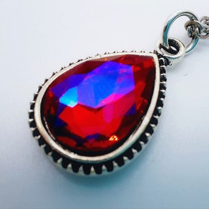 May include: A silver pendant necklace featuring a large, red, faceted teardrop-shaped gemstone.