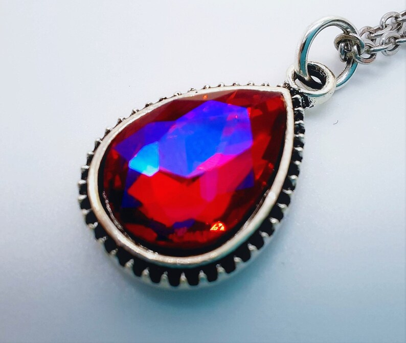 May include: A silver pendant necklace featuring a large, red, faceted teardrop-shaped gemstone.