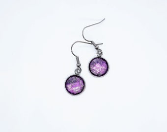 May include: A pair of silver dangle earrings with round purple and silver glitter cabochons.