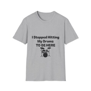 May include: A grey t-shirt featuring the text "I Stopped Hitting My Drums TO BE HERE" and a black drum kit illustration. The shirt has a crew neck and short sleeves.