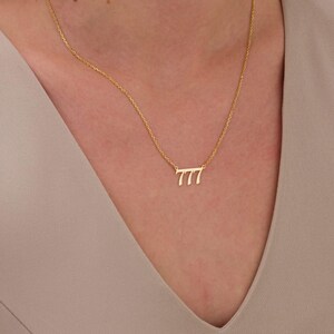 May include: A gold-toned necklace featuring a delicate chain and a pendant shaped as the number 777 in a cursive script font. The pendant is centered on the chain, which rests against the skin, showcasing a polished metallic finish throughout.