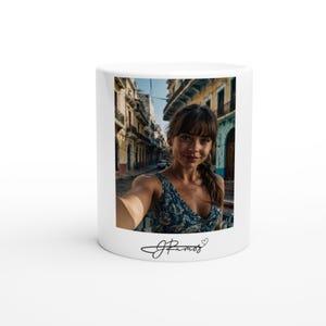 Puede incluir: Taza de cerámica blanca con un selfie de una persona con un vestido floral azul, con el fondo de una calle de la ciudad. La taza tiene una firma y un símbolo de corazón en la parte inferior.