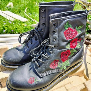 May include: Black leather boots with red rose embroidery. The boots have a yellow stitching detail around the sole.