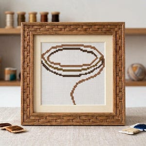 Peut inclure: Une broderie au point de croix carrée représentant un lasso marron sur un fond en tissu blanc, encadrée dans un cadre en bois texturé avec un passe-partout crème. Le lasso est réalisé avec des fils de différentes nuances de marron.