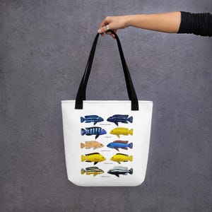 May include: White tote bag with black handles featuring a colorful illustration of different types of cichlid fish. The fish are arranged in rows and labeled with their scientific names.